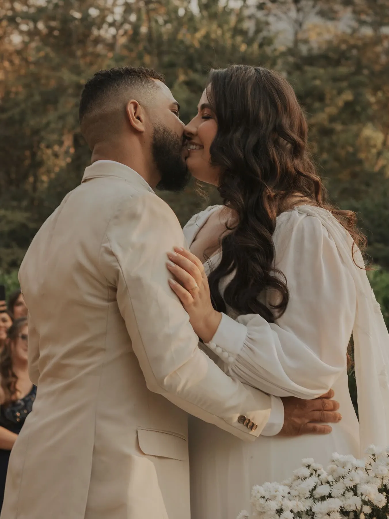 Noivos se beijando em um abraço durante casamento ao ar livre ao entardecer