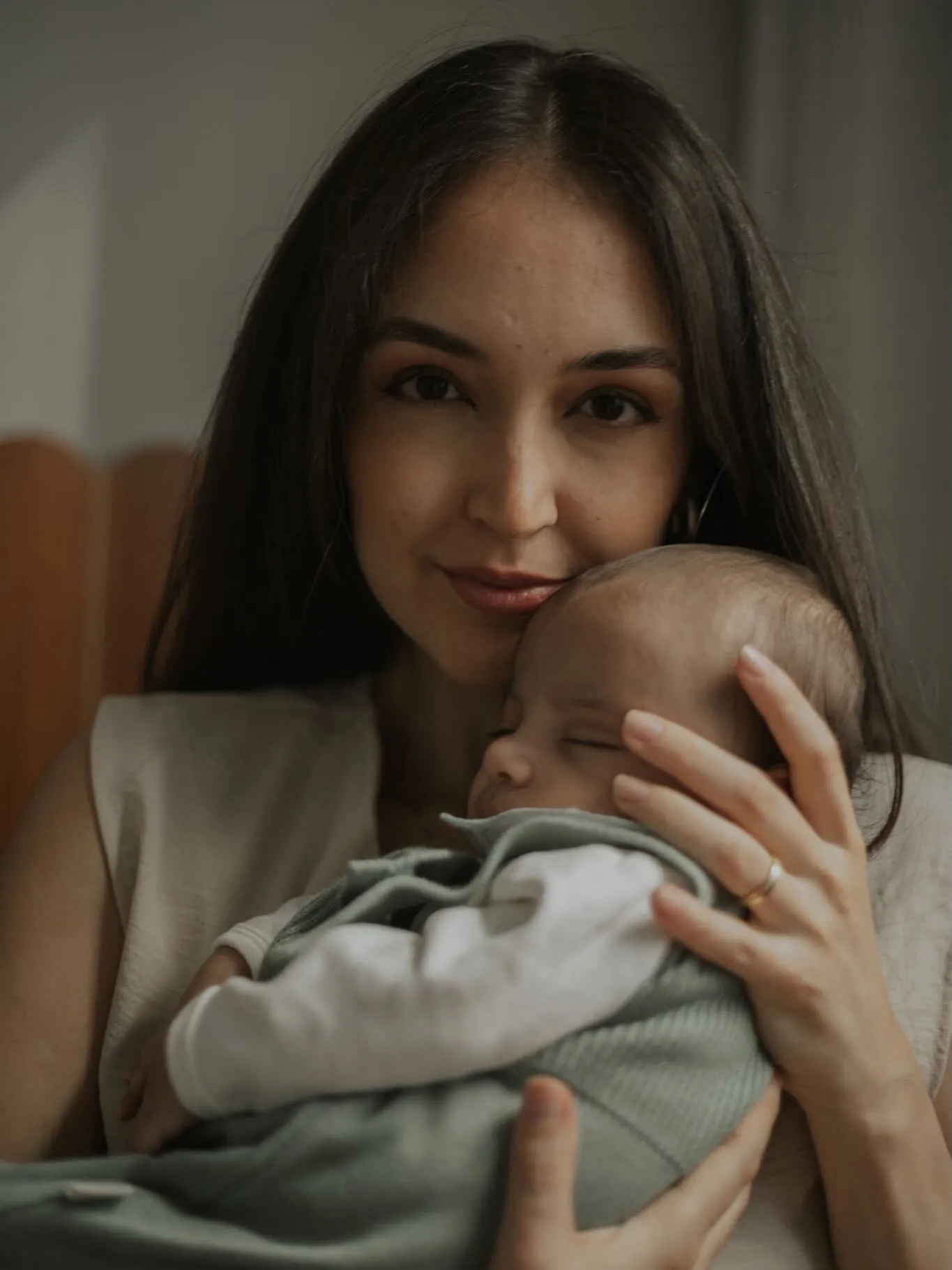 Mãe olha para a câmera segurando o bebê junto ao rosto